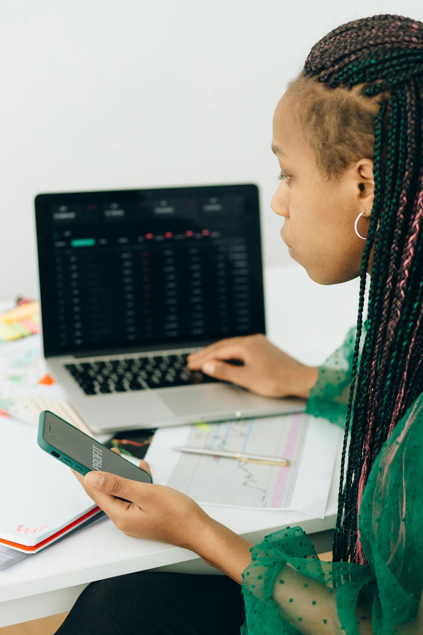 Focused woman working with financial data on laptop and smartphone in modern office.